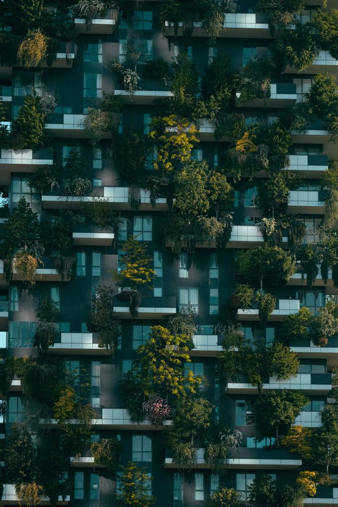 A multi-story building features balconies heavily planted with lush green trees and shrubs.