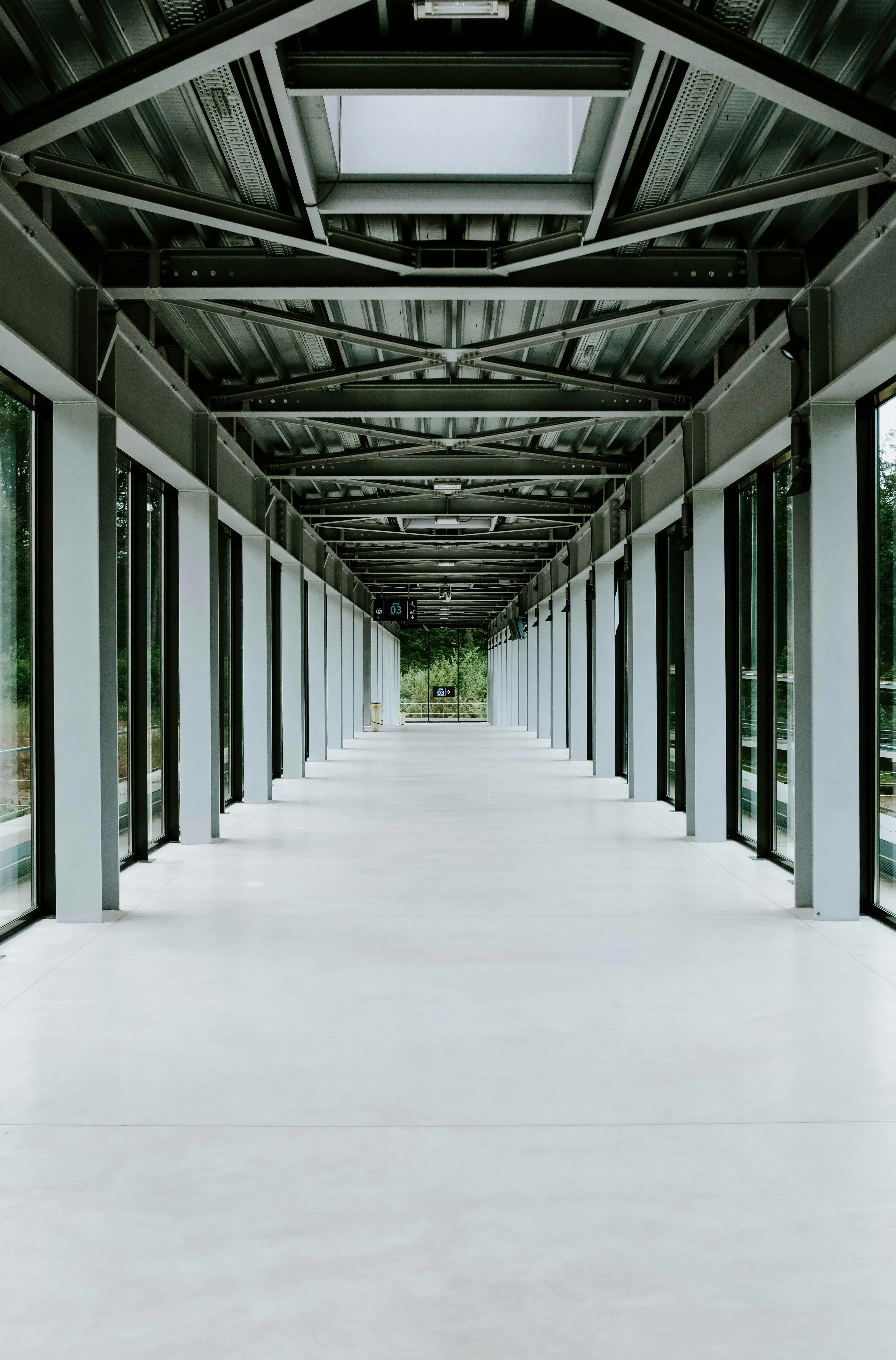 A long, modern hallway with glass walls and a metal ceiling creating strong linear perspective.