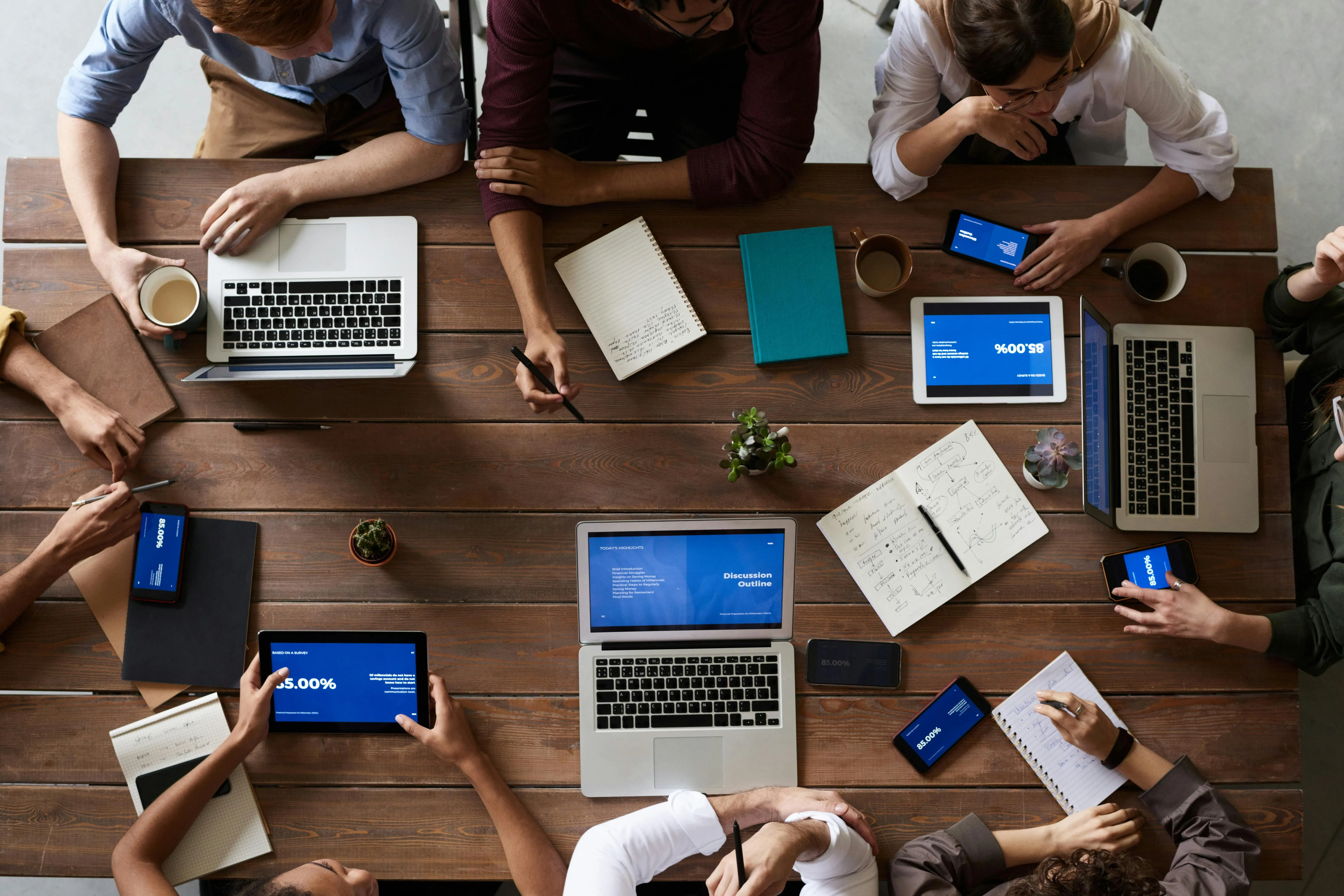 Overhead view of people collaborating around a wooden table with laptops and tablets.