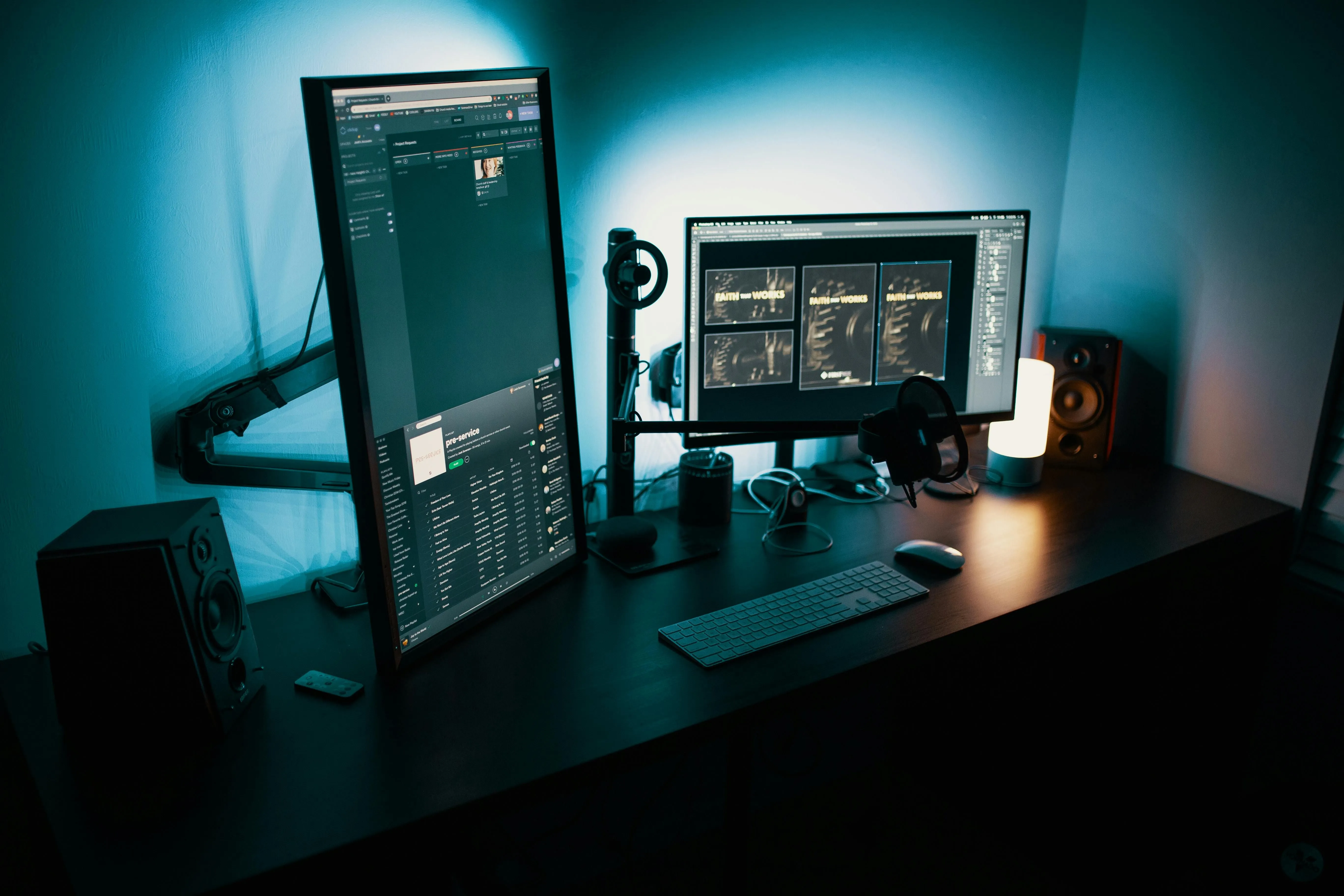 Dual computer monitors on a dark desk displaying creative software, illuminated by blue light.